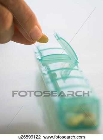 Stock Image - Man reaching for medication in pill organizer. Fotosearch