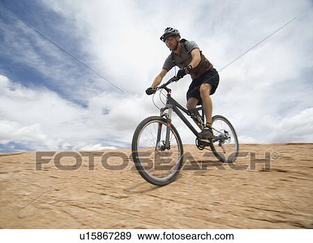 Stock Photo - Man riding mountain bike on rock formation. Fotosearch