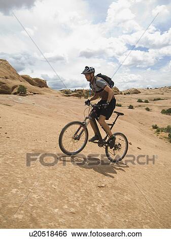Stock Photograph - Man riding mountain bike on rock formation. Fotosearch