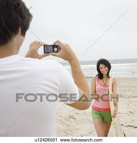 Man taking photograph of girlfriend with surfboard at beach View Large Photo Image Stock Image - Man taking photograph of girlfriend with surfboard at beach. Fotosearch