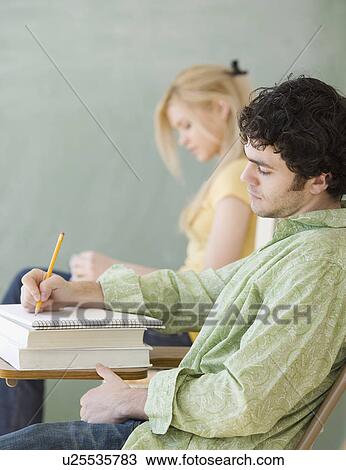Stock Image - Man writing at desk in classroom. Fotosearch
