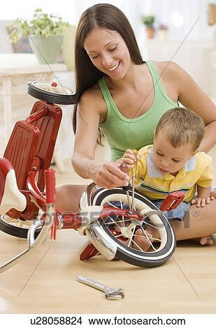 Picture - Mother holding baby and fixing tricycle. Fotosearch