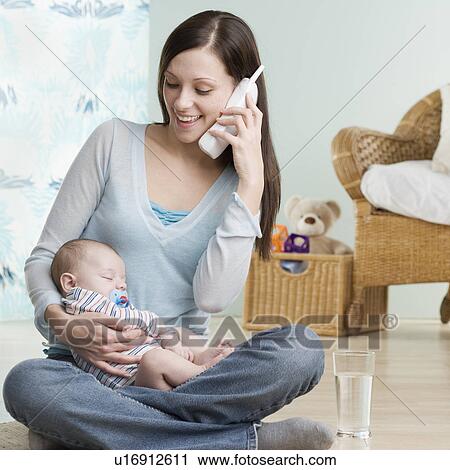 Stock Image - Mother on telephone with sleeping baby in her lap. Fotosearch