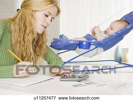 Stock Photo - Mother using calculator with baby in seat on table. Fotosearch