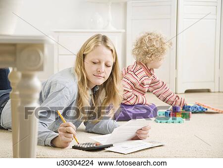 Mother working on calculator while child plays View Large Photo Image Picture - Mother working on calculator while child plays. Fotosearch