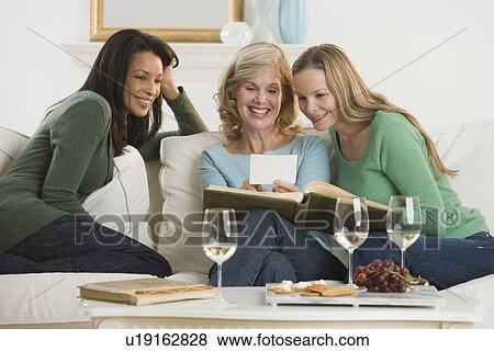 Stock Photo - Multi-ethnic women looking at photo album. Fotosearch