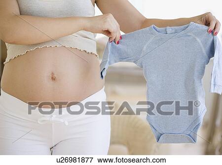 Stock Photo - Pregnant woman holding baby clothes. Fotosearch
