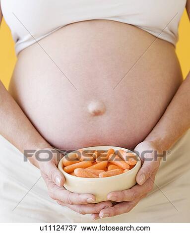 Pregnant woman holding bowl of carrots View Large Photo Image Stock Photo - Pregnant woman holding bowl of carrots. Fotosearch