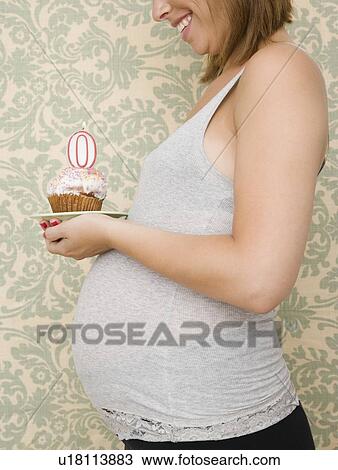 Stock Image - Pregnant woman holding cupcake with zero candle. Fotosearch