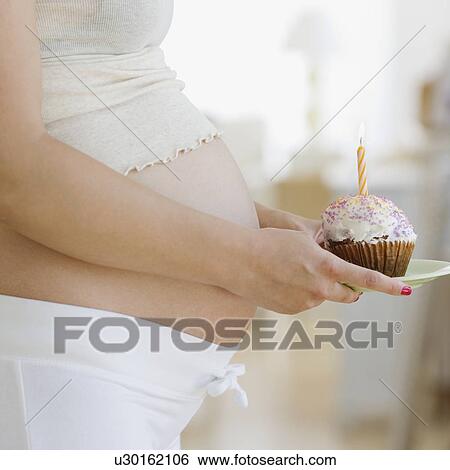 Stock Photograph - Pregnant woman holding cupcake with candle. Fotosearch