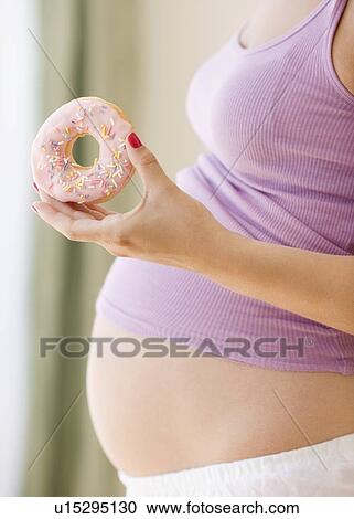 Stock Image - Pregnant woman holding donut. Fotosearch