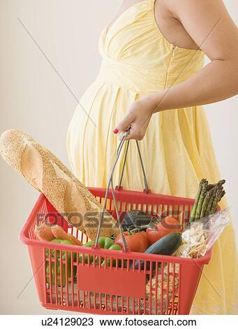 Stock Image - Pregnant woman holding grocery basket. Fotosearch