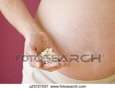 Stock Photo - Pregnant woman holding handful of vitamins. Fotosearch