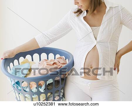 Stock Image - Pregnant woman holding laundry basket. Fotosearch