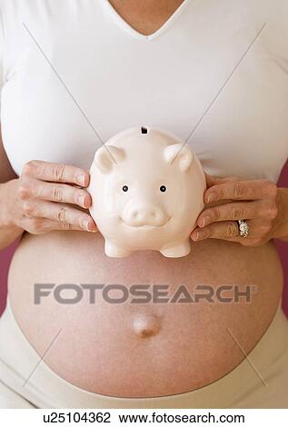 Stock Image - Pregnant woman holding piggy bank. Fotosearch
