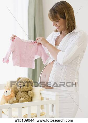 Pregnant woman holding up baby clothing View Large Photo Image Picture - Pregnant woman holding up baby clothing. Fotosearch