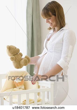Stock Photo - Pregnant woman smiling at teddy bear. Fotosearch