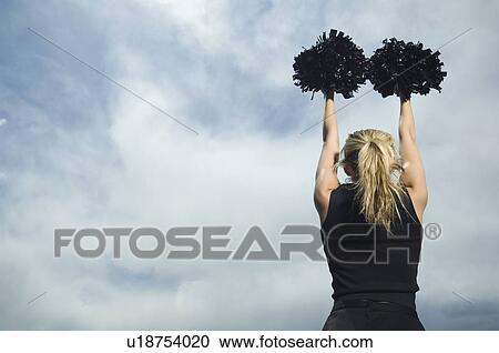 Stock Image - Rear view of cheerleader with pom poms. Fotosearch
