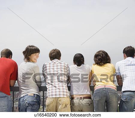 Stock Image - Rear view of friends with woman looking over shoulder. Fotosearch