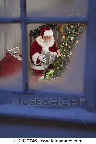 Santa Claus leaving gifts under Christmas tree View Large Photo Image Stock Photograph - Santa Claus leaving gifts under Christmas tree. Fotosearch
