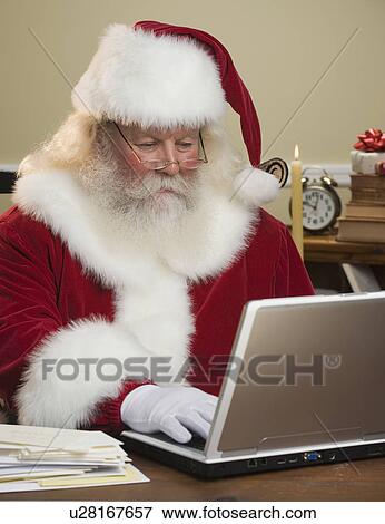 Stock Photo - Santa Claus looking at laptop. Fotosearch