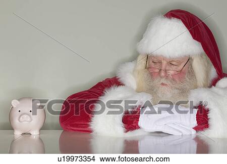Picture - Santa Claus looking at piggy bank. Fotosearch