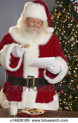 Stock Photo - Santa Claus reading letter and eating cookies. Fotosearch