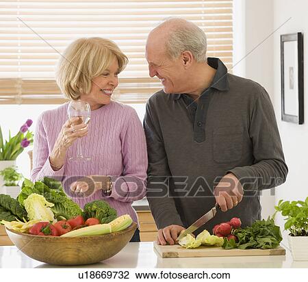 Stock Image - Senior couple chopping vegetables and drinking wine. Fotosearch