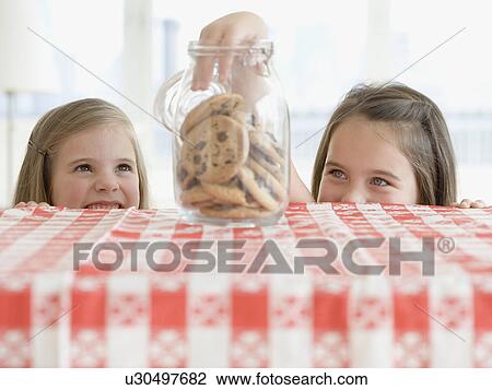 Stock Image - Sisters taking cookies from jar. Fotosearch