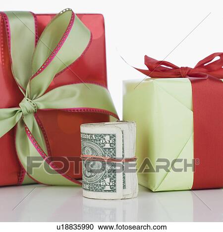 Stock Image - Studio shot of roll of dollar bills and gifts. Fotosearch