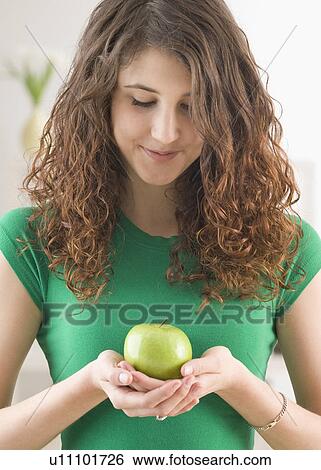 Teenage girl holding apple and looking down View Large Photo Image Stock Photograph - Teenage girl holding apple and looking down. Fotosearch