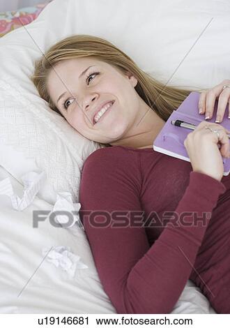 Stock Image - Teenage girl holding journal on bed. Fotosearch