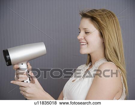 Stock Photo - Teenage girl pointing hair dryer at face. Fotosearch