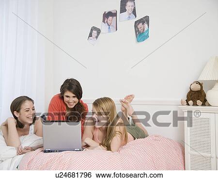 Teenage girls looking at laptop on bed View Large Photo Image Stock Photograph - Teenage girls looking at laptop on bed. Fotosearch