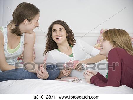 Stock Image - Teenage girls playing cards on bed. Fotosearch