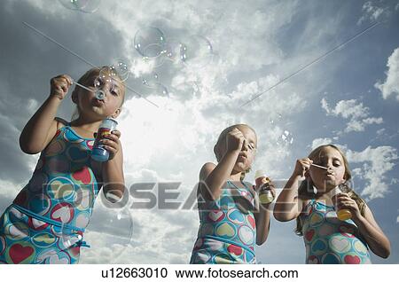 Stock Image - Three young sisters blowing bubbles. Fotosearch