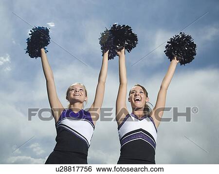 Stock Photograph - Two cheerleaders holding pom poms over head. Fotosearch