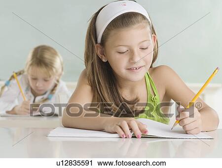 Stock Image - Two young girls writing at desks. Fotosearch