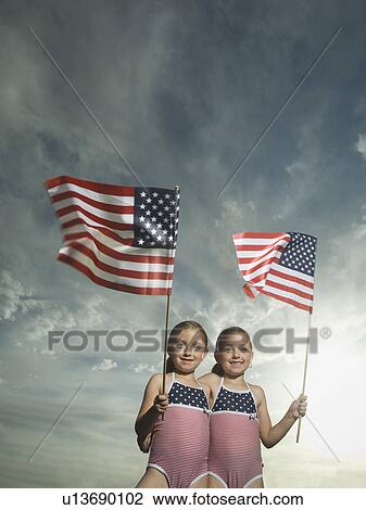 Stock Image - Two young sisters holding American flags. Fotosearch