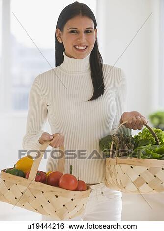 Stock Photograph - Woman carrying baskets of fruit and vegetables. Fotosearch