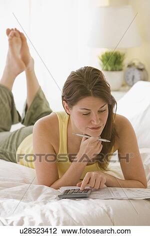 Stock Image - Woman doing finances on bed. Fotosearch