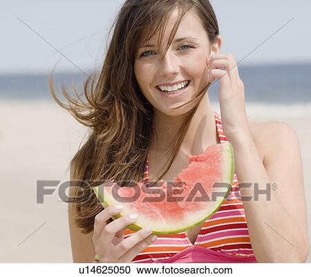 Stock Image - Woman eating watermelon at beach. Fotosearch