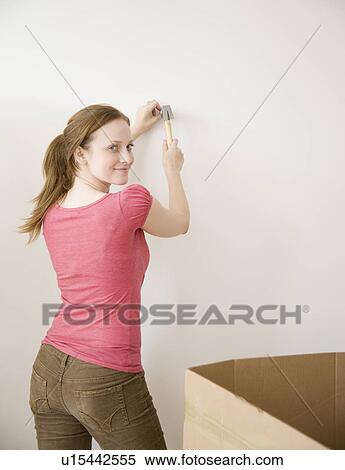 Stock Photography - Woman hammering nail in wall. Fotosearch