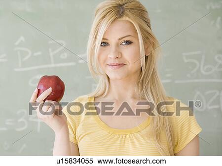 Stock Photography - Woman holding apple in front of blackboard. Fotosearch