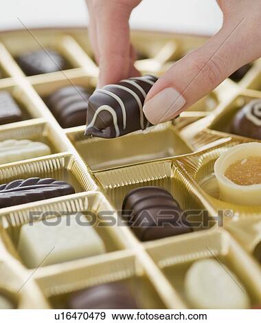 Stock Photo - Woman holding chocolate over box of chocolates. Fotosearch