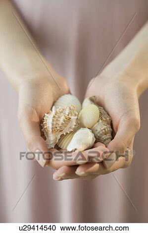Stock Image - Woman holding handful of seashells. Fotosearch