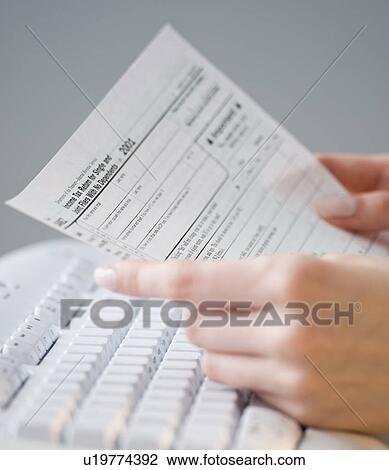 Stock Image - Woman holding tax form over keyboard. Fotosearch
