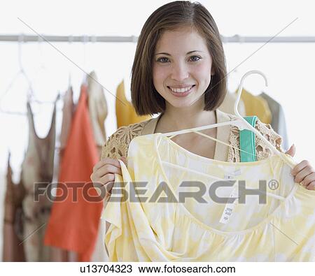 Woman holding up shirt in clothing store View Large Photo Image Stock Image - Woman holding up shirt in clothing store. Fotosearch