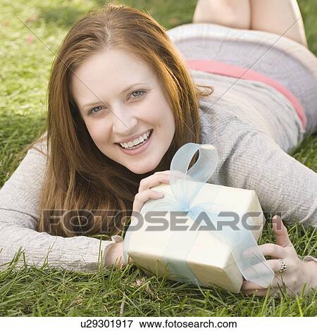 Woman laying in grass holding gift View Large Photo Image Stock Photo - Woman laying in grass holding gift. Fotosearch