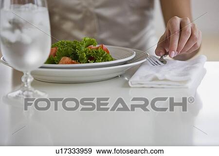 Stock Photo - Woman lifting fork next to plate of food. Fotosearch